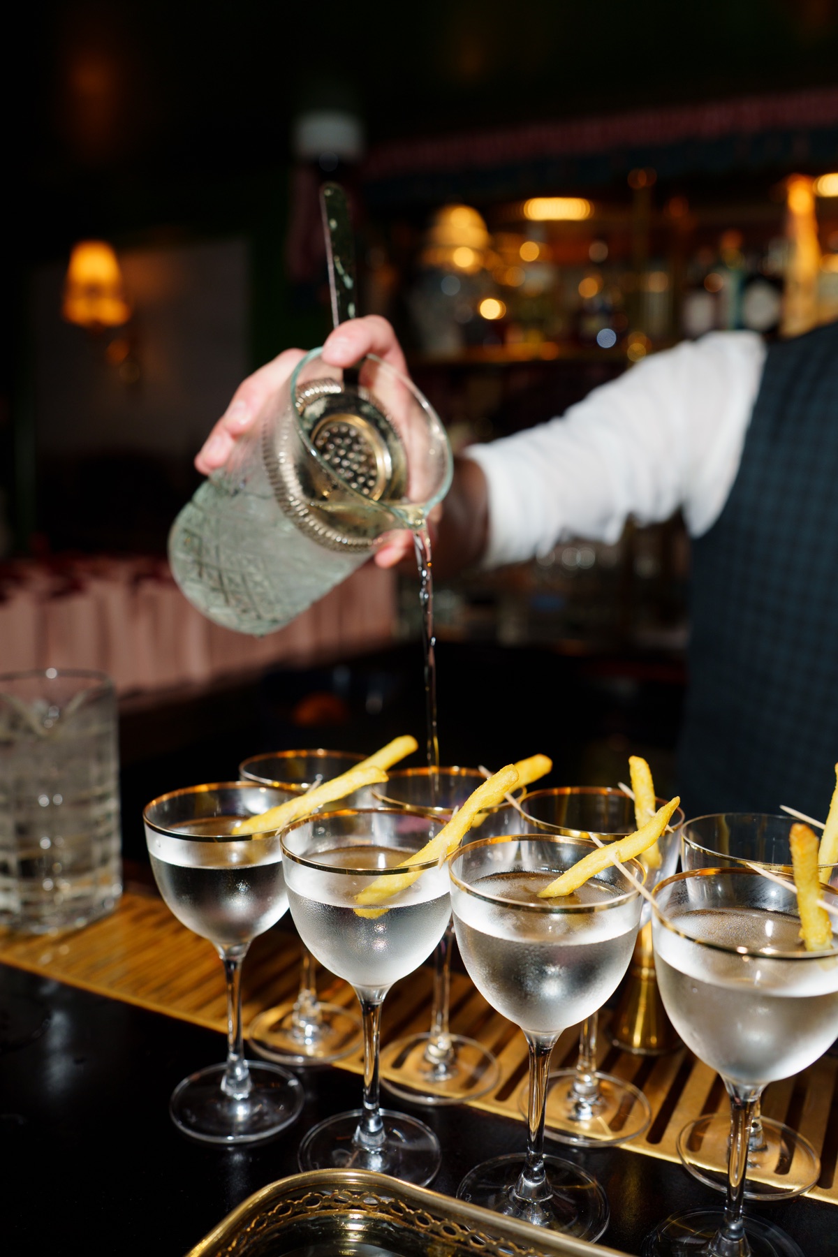 A bartender pouring a row of beautifully presented drinks